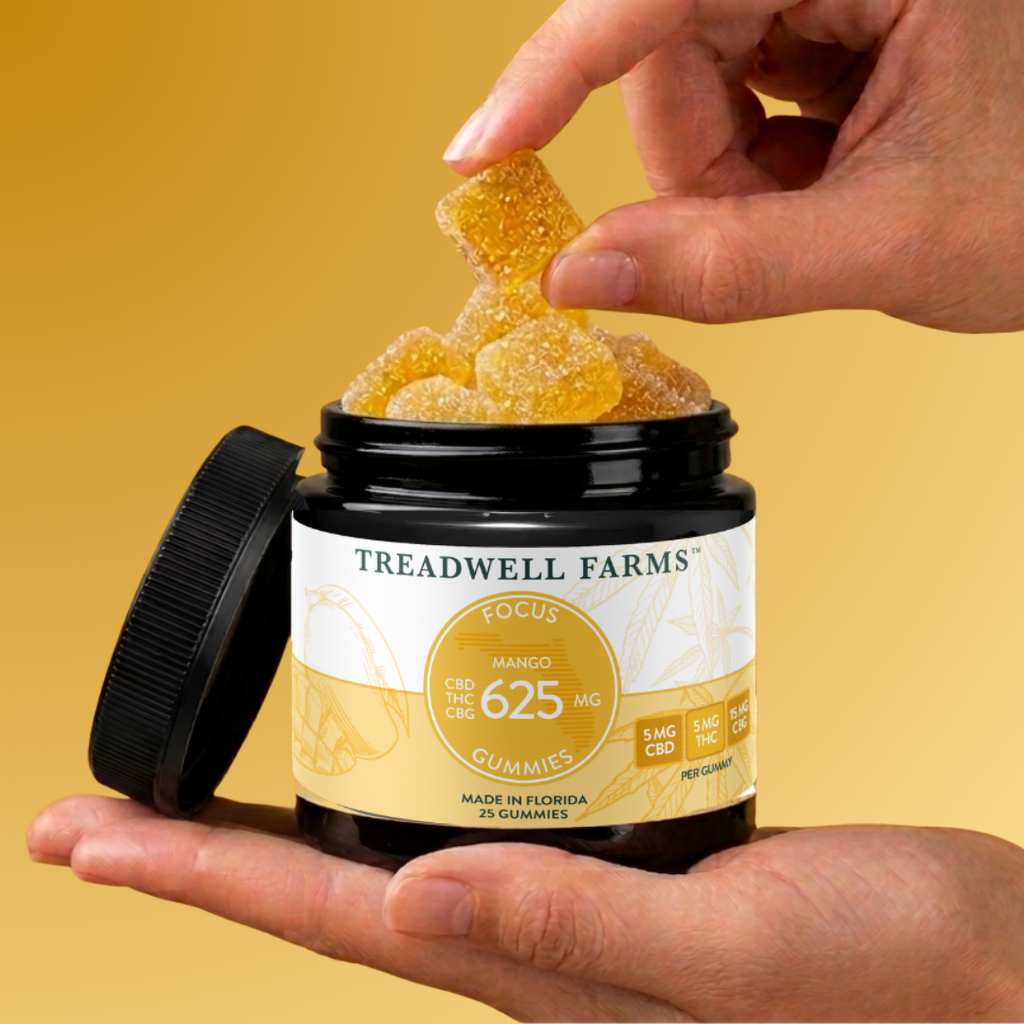 A jar of Treadwell Farms Focus Gummies held in a hand, with another hand lifting several translucent yellow gummy candies from the open jar against a warm yellow background.
