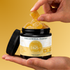 A jar of Treadwell Farms Focus Gummies held in a hand, with another hand lifting several translucent yellow gummy candies from the open jar against a warm yellow background.