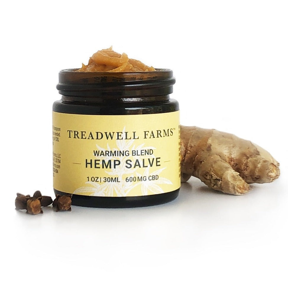 Open jar of Treadwell Farms 600 mg CBD Warming Blend Hemp Salve displaying salve texture propped with cloves and ginger